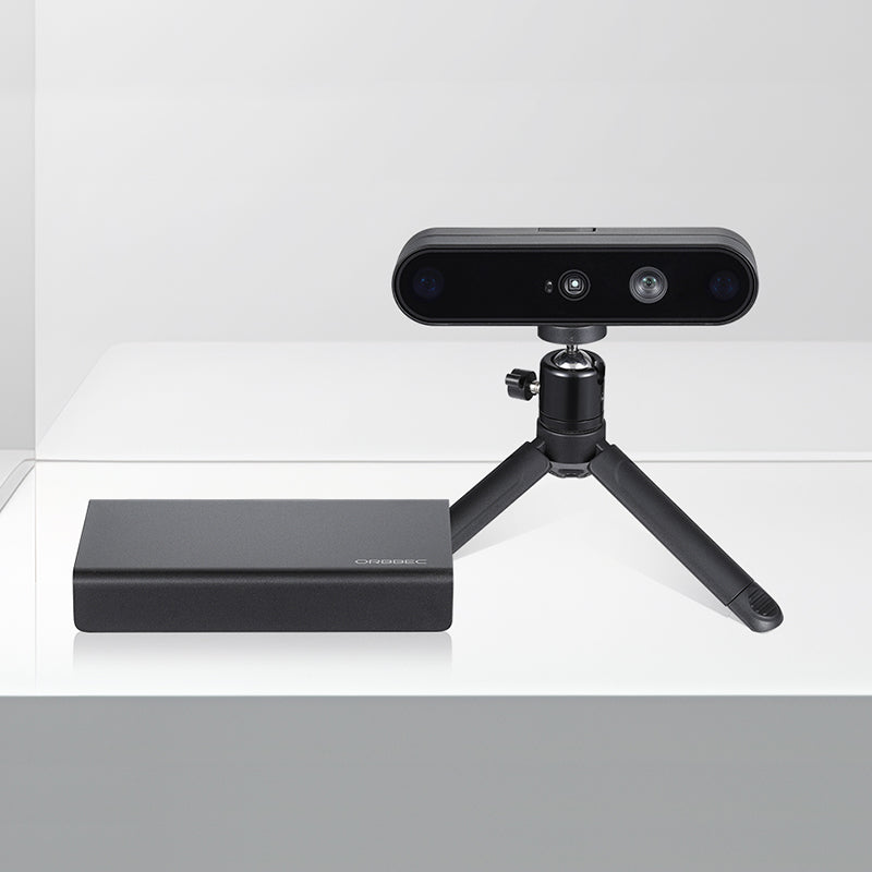 Front view of Orbbec Gemini 2 XL 3D camera on a mini tripod placed alongside the sleek black OBox PoE adapter.